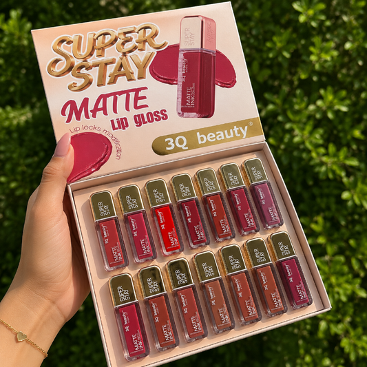 Box of 3Q Beauty Super Stay Matte Lip Glosses with lip glosses displayed in front against a green leafy background.
