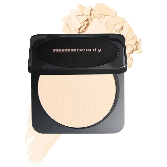 Huda Beauty compact powder with a scoop of powder on a white background