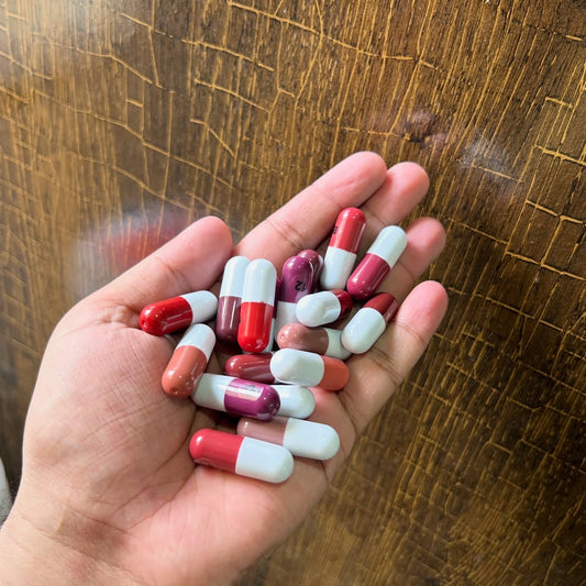 A hand holding several red and white capsules against a textured wooden background.