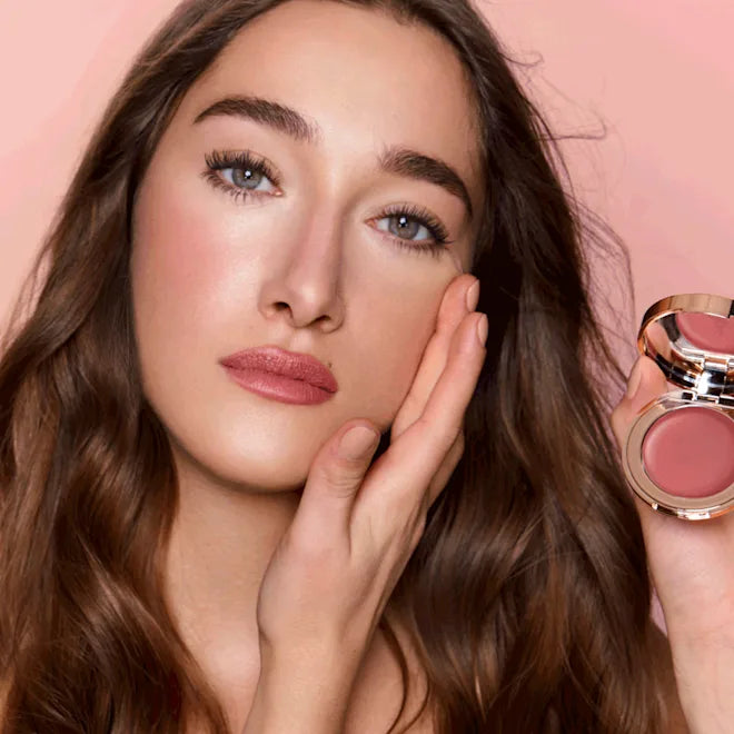 Woman holding a makeup product with a pink background