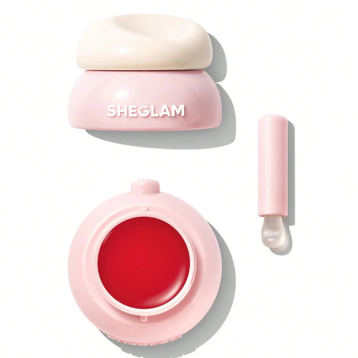 Pink cosmetic container with red substance and applicator on a white background, featuring the brand 'SHEGLAM'.